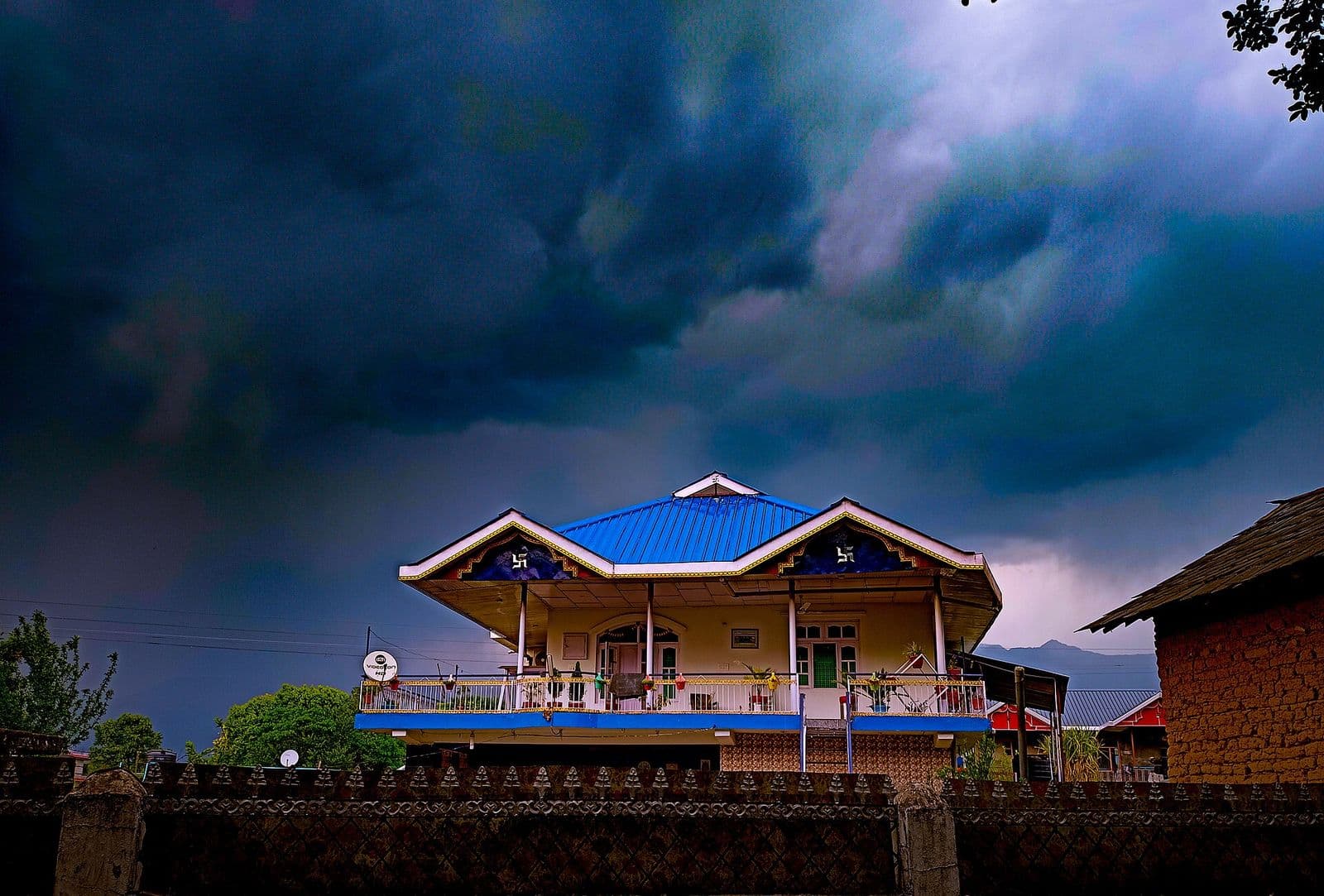 Blue-roofed village house under stormy skies in Andretta artists' village, Kangra