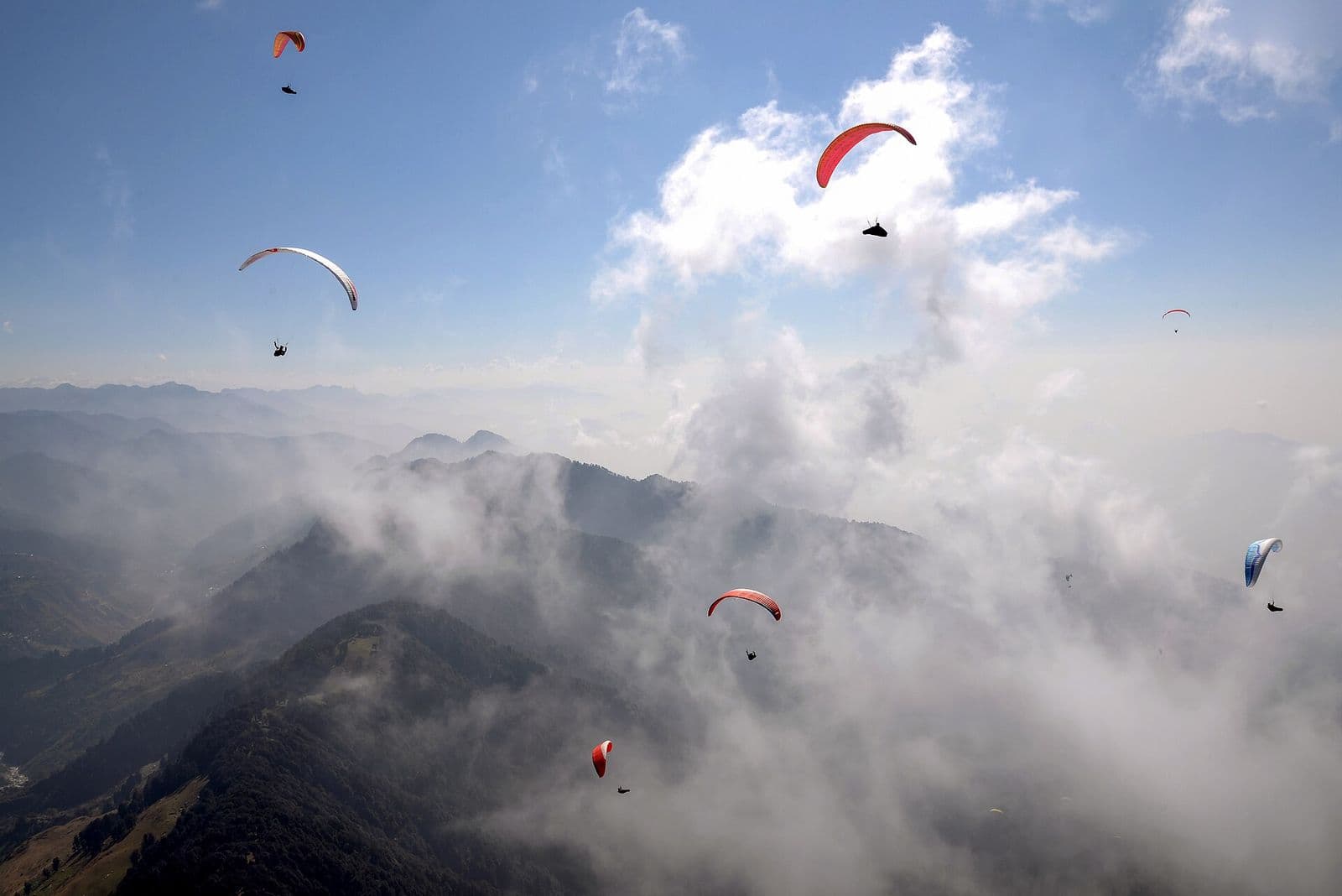 Paragliders soaring above clouds and mountain ridges at Bir Billing