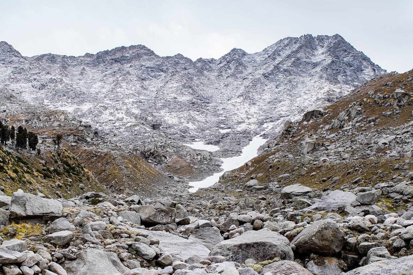 Boulder-strewn trail and snow-dusted Dhauladhar ridge looking up towards Indrahar Pass