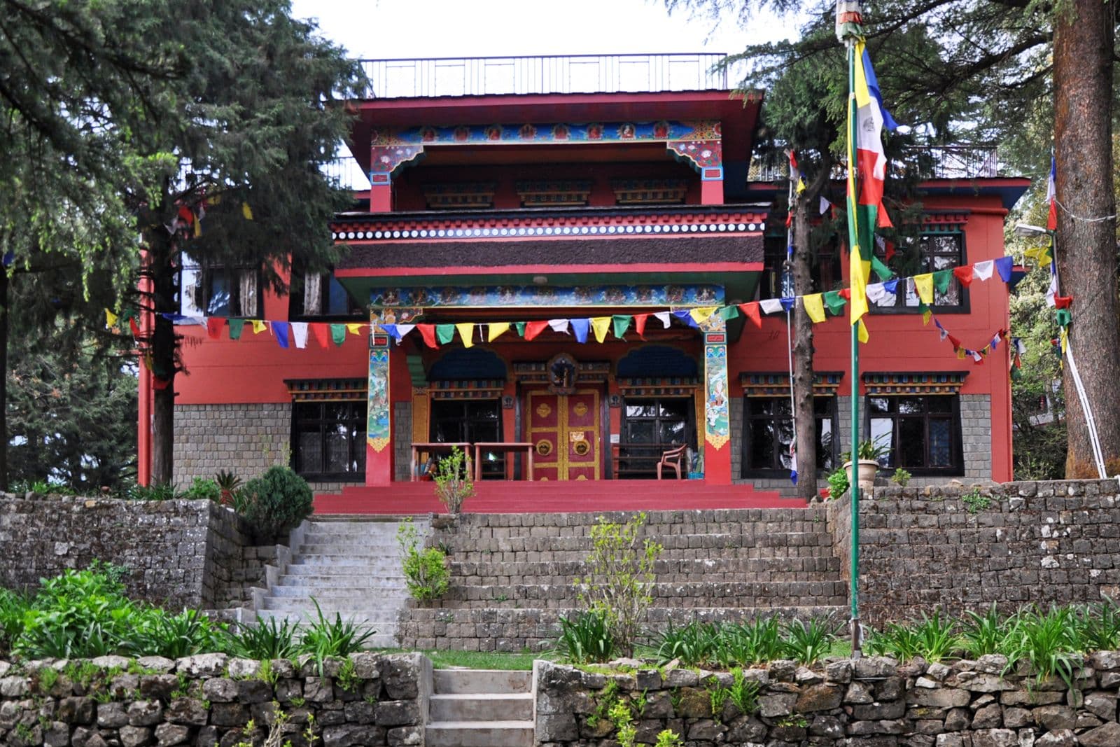 Main gompa of Tushita Meditation Centre in Dharamkot, a red Tibetan-style hall among cedar trees