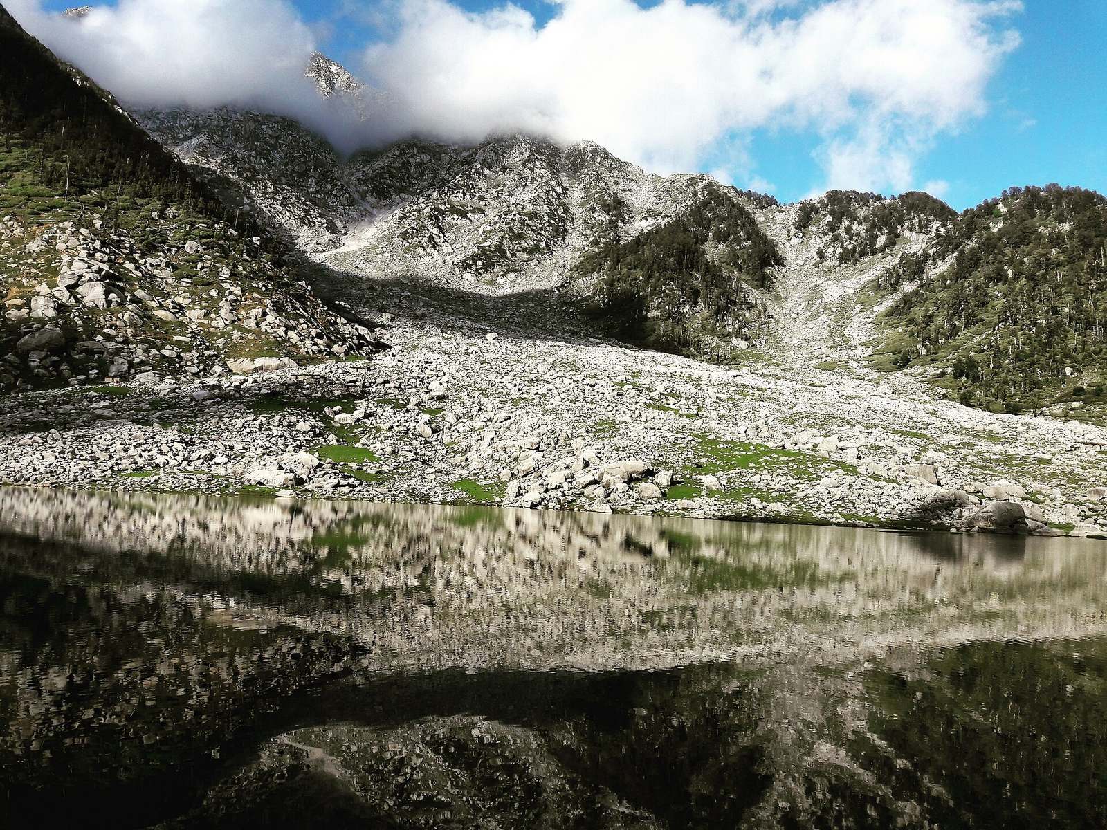 Kareri Lake (Kareri Dal) mirroring the boulder-strewn Dhauladhar slopes below the Minkiani Pass
