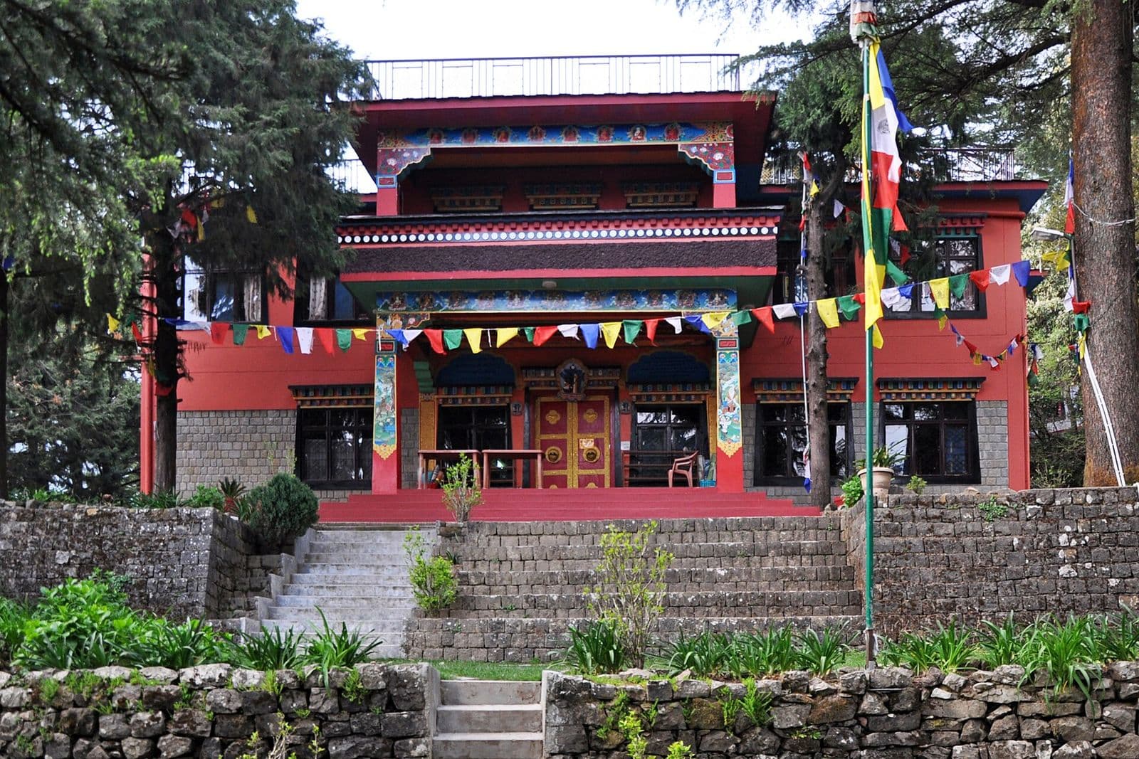 Red-and-gold main gompa of Tushita Meditation Centre among trees and prayer flags in Dharamkot