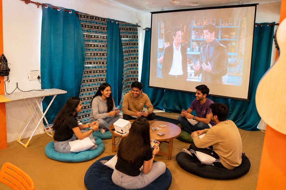 Common room with projector screen and floor seating at Loopin McLeodganj