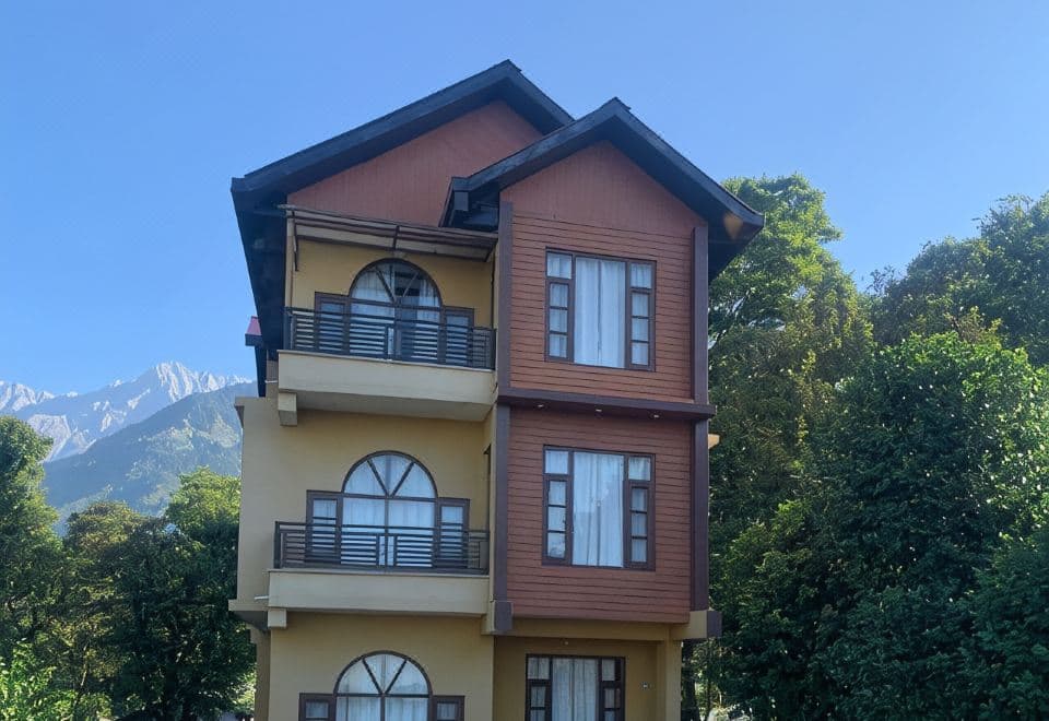Timber-clad three-storey block at The Sojourn with arched windows and the Dhauladhar peaks behind