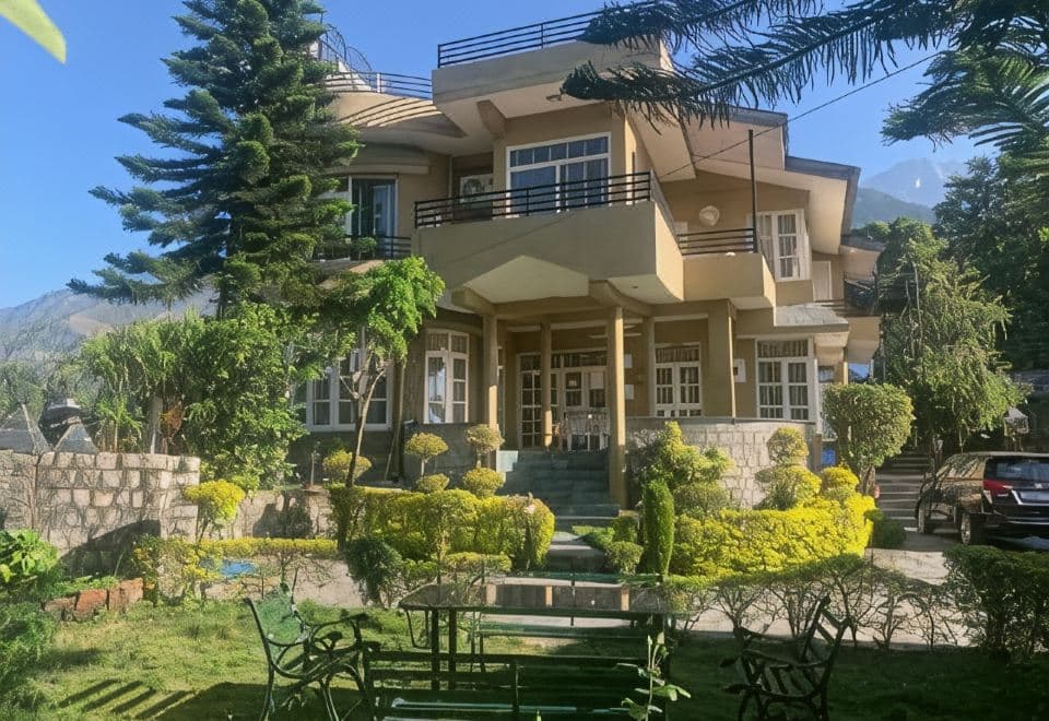 Main cottage of The Sojourn with balconies, behind a landscaped lawn with garden benches, near Norbulingka