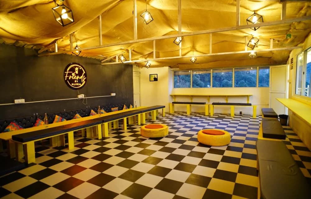 Long common hall with yellow benches, pouf seats, the Friends by Alizeh neon sign and windows along one wall