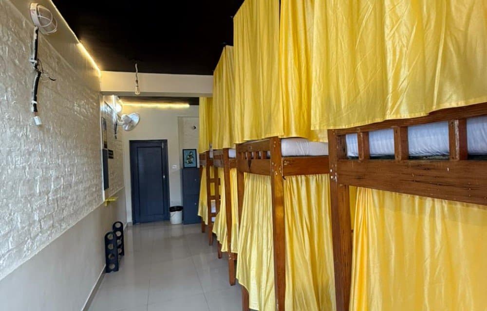 Dorm room with a row of wooden bunk beds, each with yellow privacy curtains