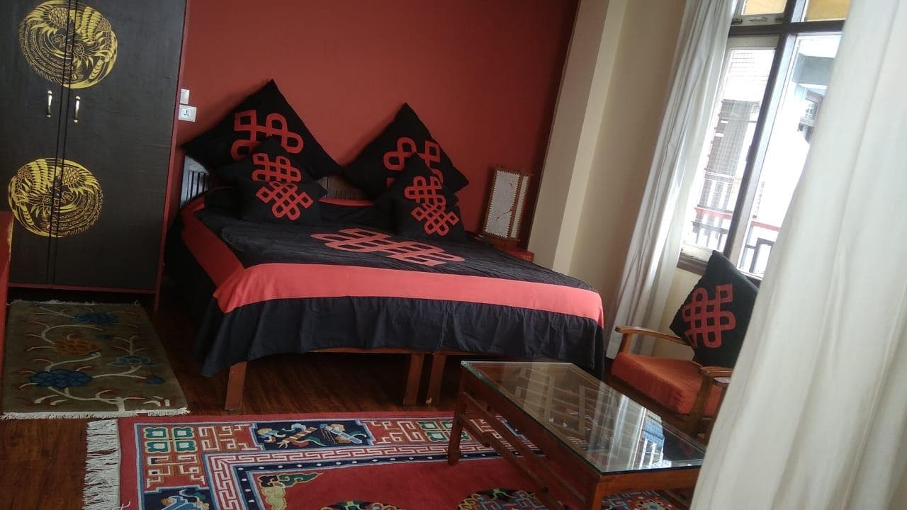 Double room with endless-knot cushions and Tibetan rugs at Serkong House, Nowrojee Road, McLeod Ganj