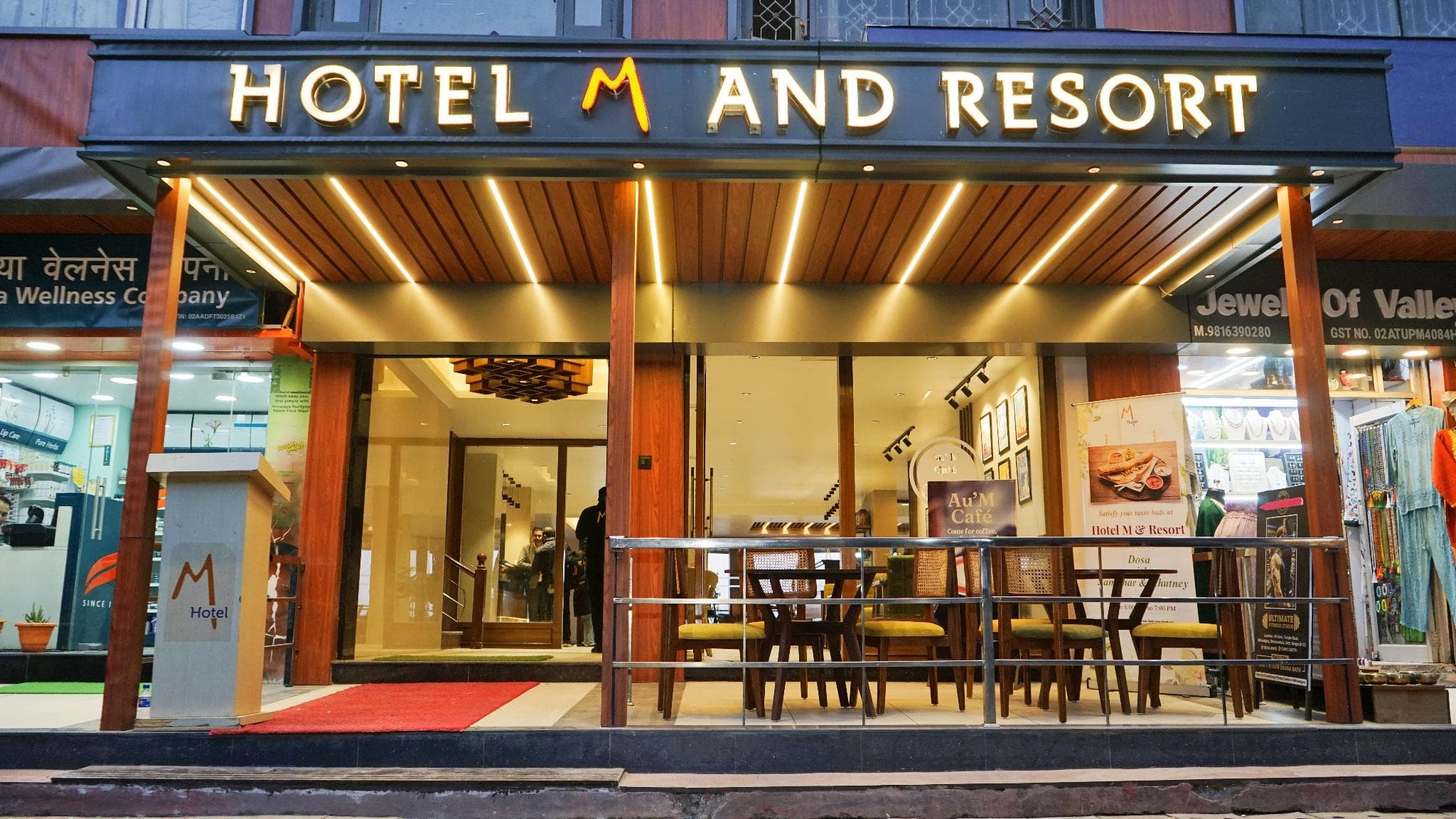 Lit entrance and café seating under the Hotel M and Resort sign on Dalai Lama Temple Road, McLeod Ganj