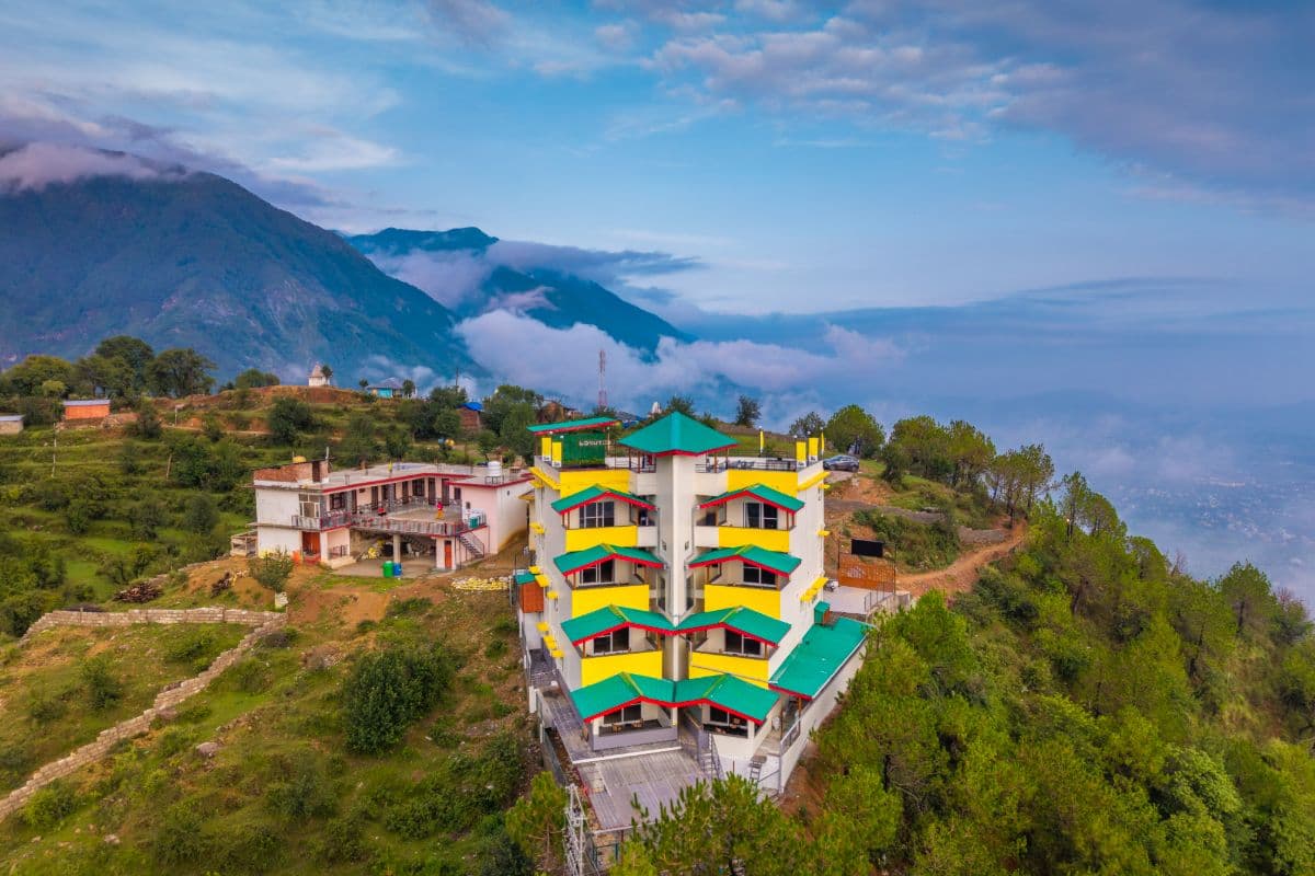 The Hosteller Dharamshala building on a hilltop in Bangatu village with valley and Dhauladhar views