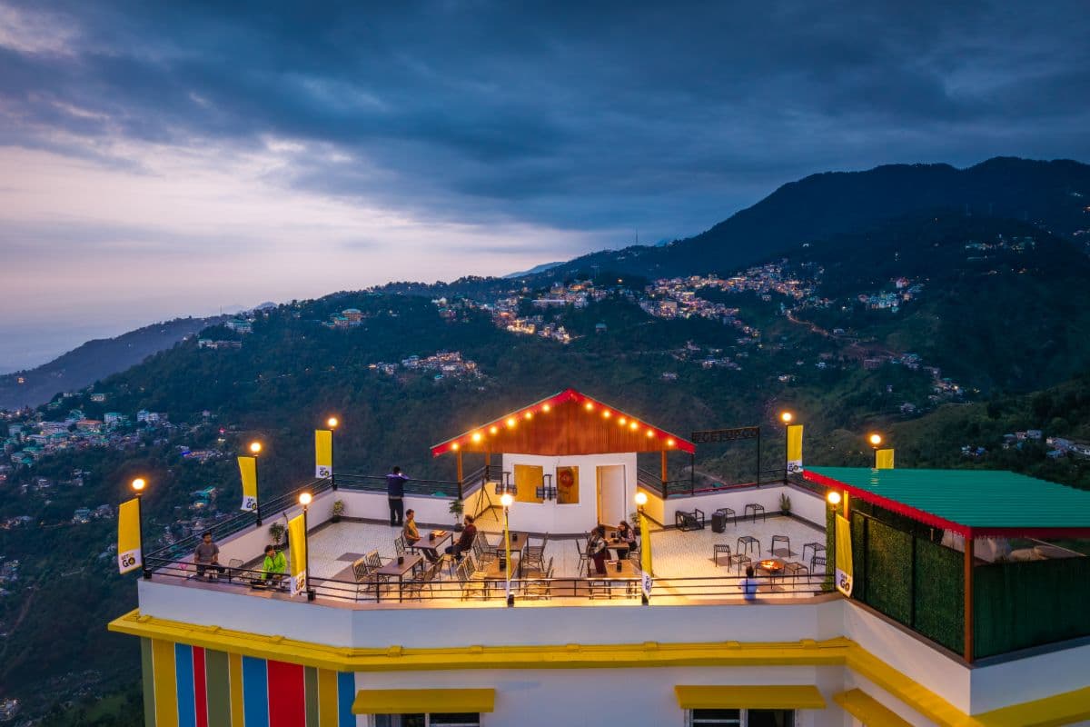 Rooftop of The Hosteller Dharamshala at dusk with the hillside lights behind