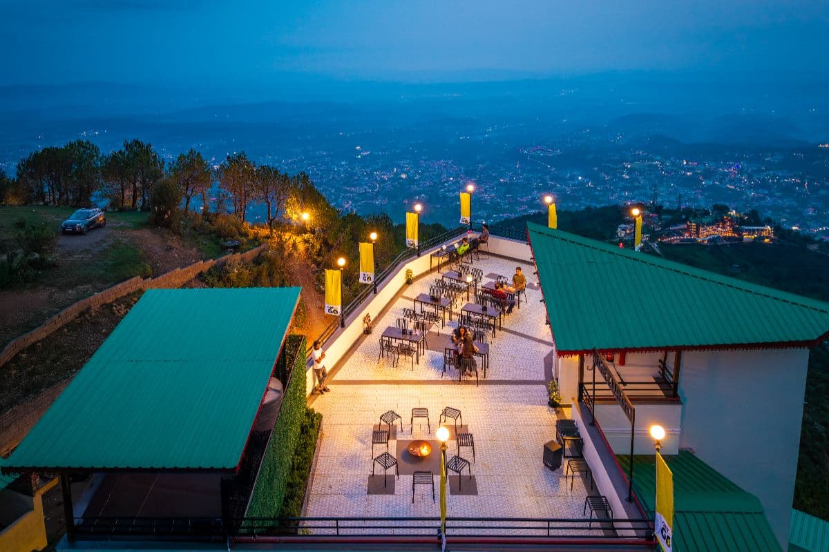 Rooftop cafe terrace at The Hosteller Dharamshala lit up at dusk over the valley