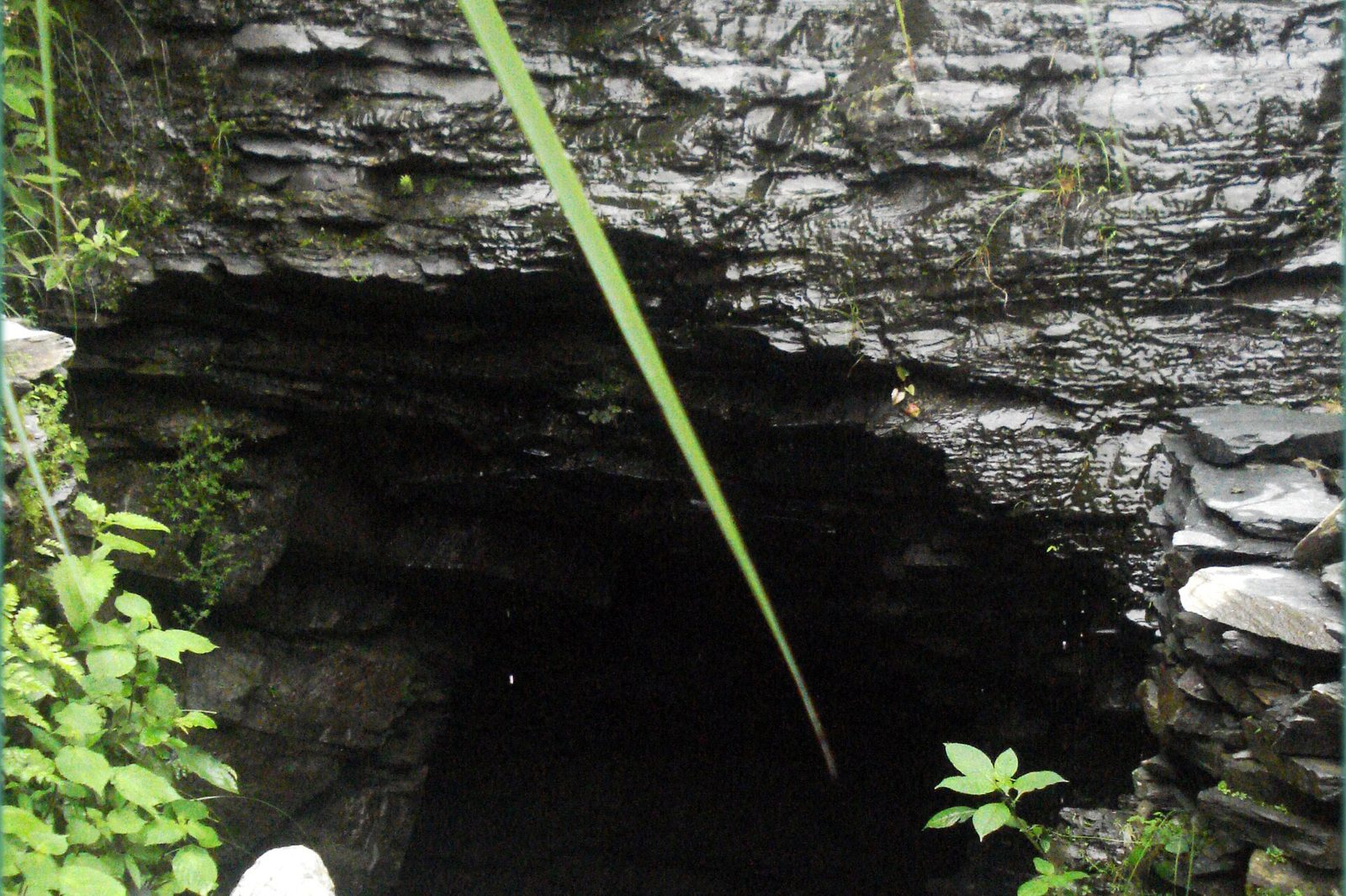Dark opening of a slate mine cut into thinly layered grey slate at Khaniyara, Dharamshala, with slate waste below