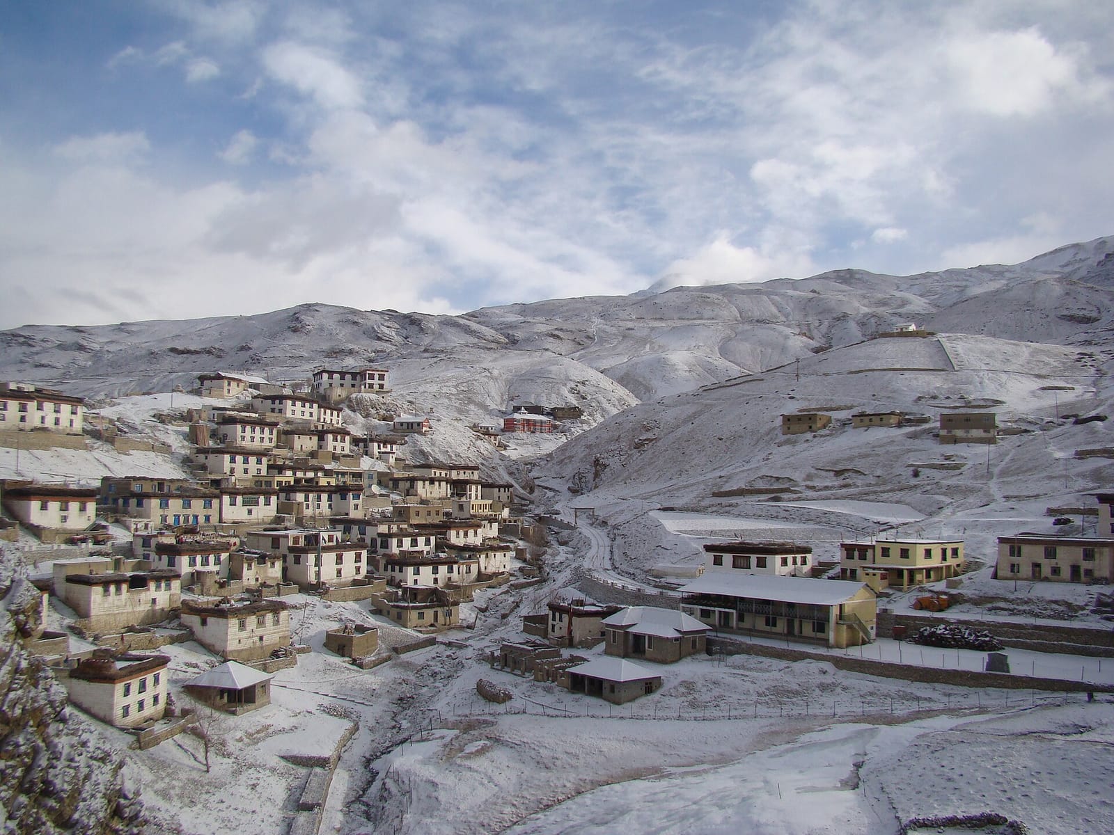 Kibber village in Spiti under fresh snow, white-walled houses climbing a hillside below snowy slopes