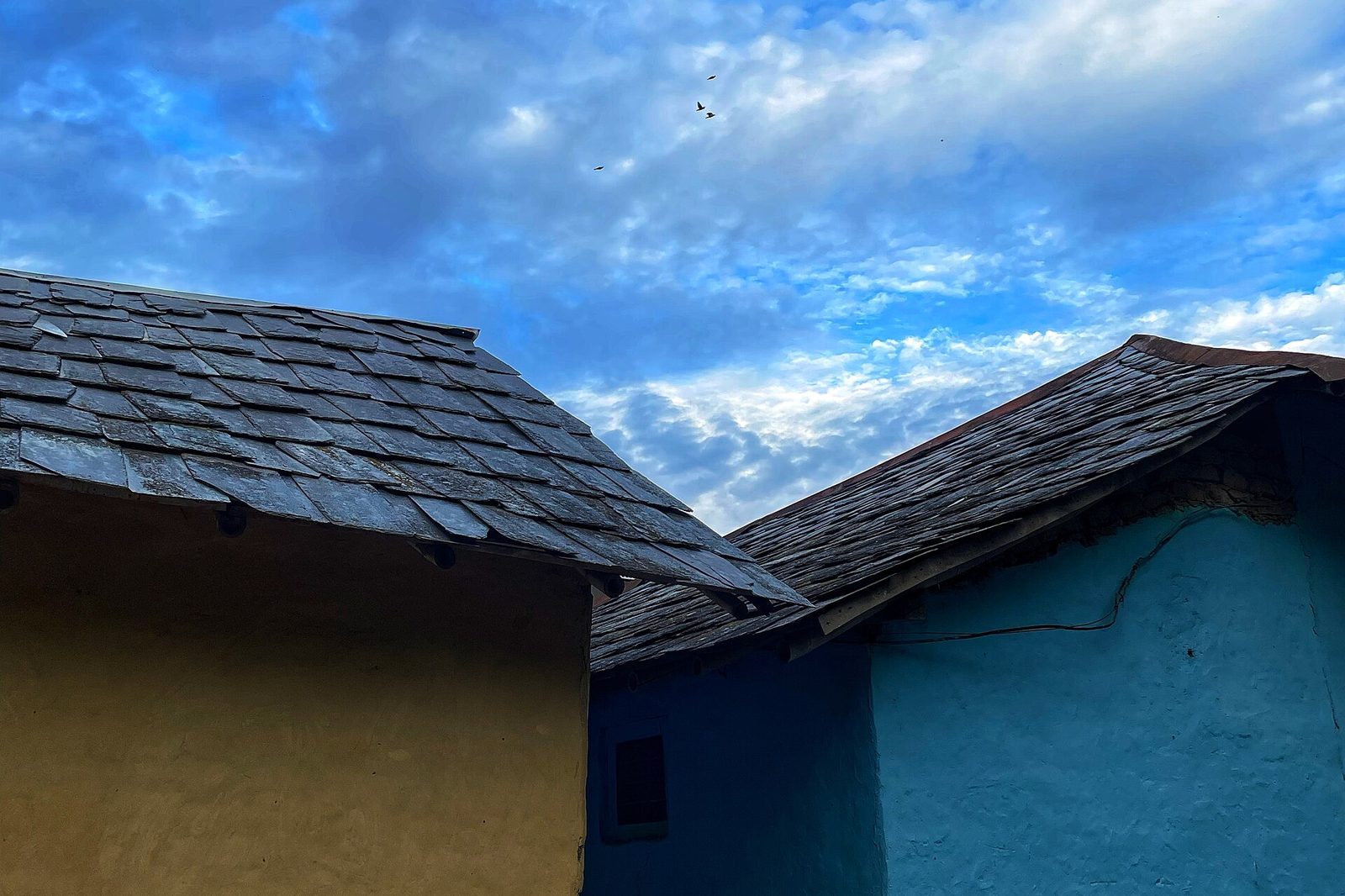Grey slate-tiled roofs on blue and ochre mud-plastered houses in Naura village, Kangra district